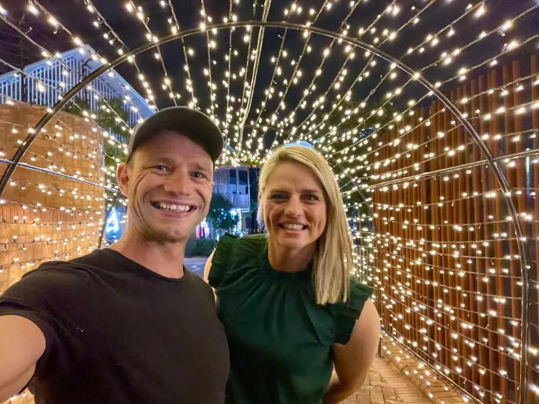 Christiaan and Corinne in a tunnel of fairy lights at night, him in a black cap and T-shirt, her in a green top.